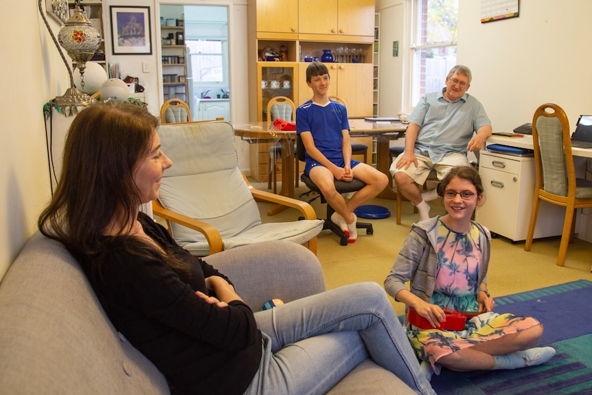 a family sitting down and looking and talking to a young girl sitting on the floor