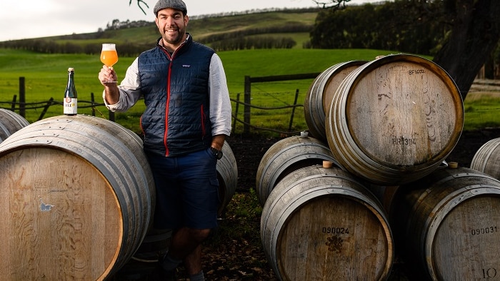Man stands outside among large barrels holds a glass of beer on wintery day