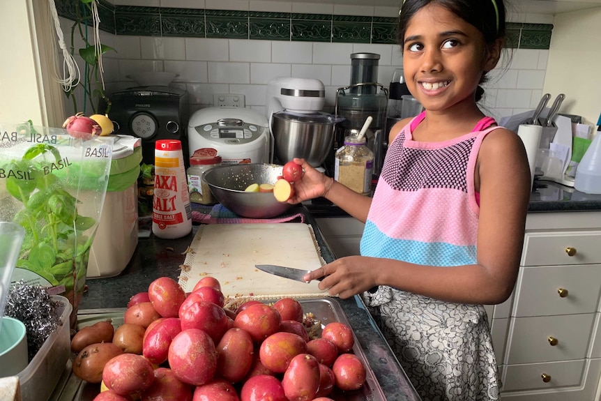 Diya smiles while preparing potatoes, for a story about her charity with her father during Melbourne's lockdown.