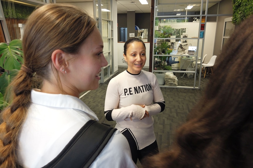 A petite dance teacher talks to some students in a studio