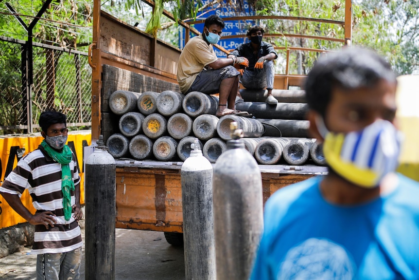 I lavoratori siedono su un camion carico di bombole di ossigeno per un ospedale di Nuova Delhi, in India.