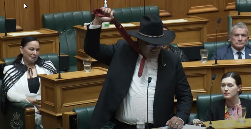 A man holding his tie up above his head in new Zealand parliament.