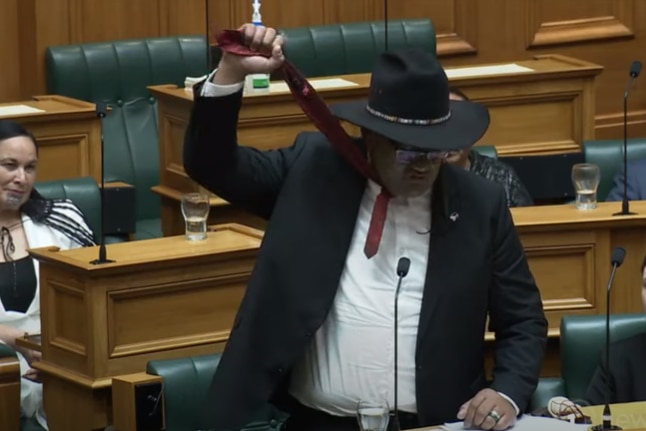 A man holding his tie up above his head in new Zealand parliament.