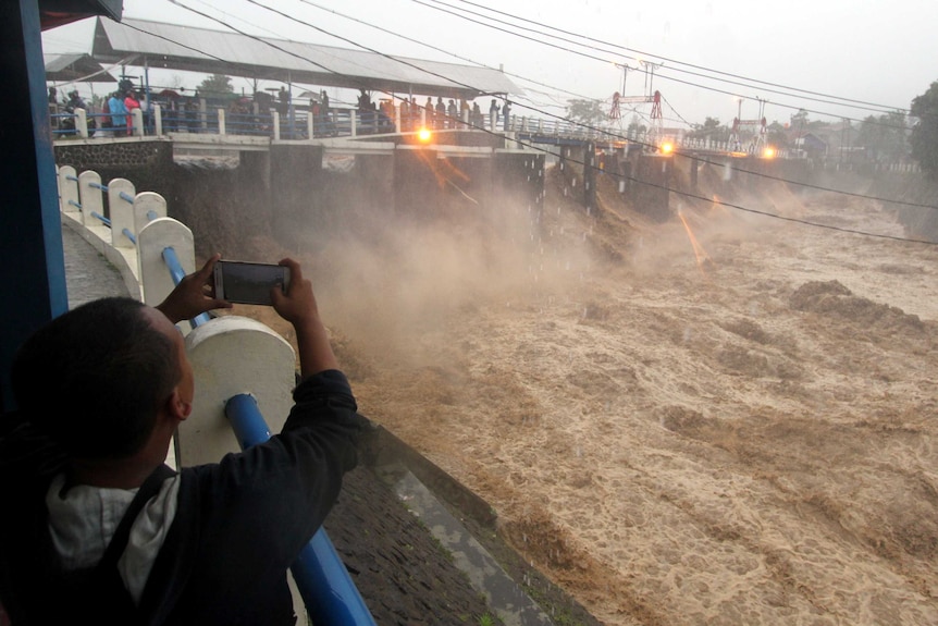Residents watch muddy turbulent water rushing below in Bogor City