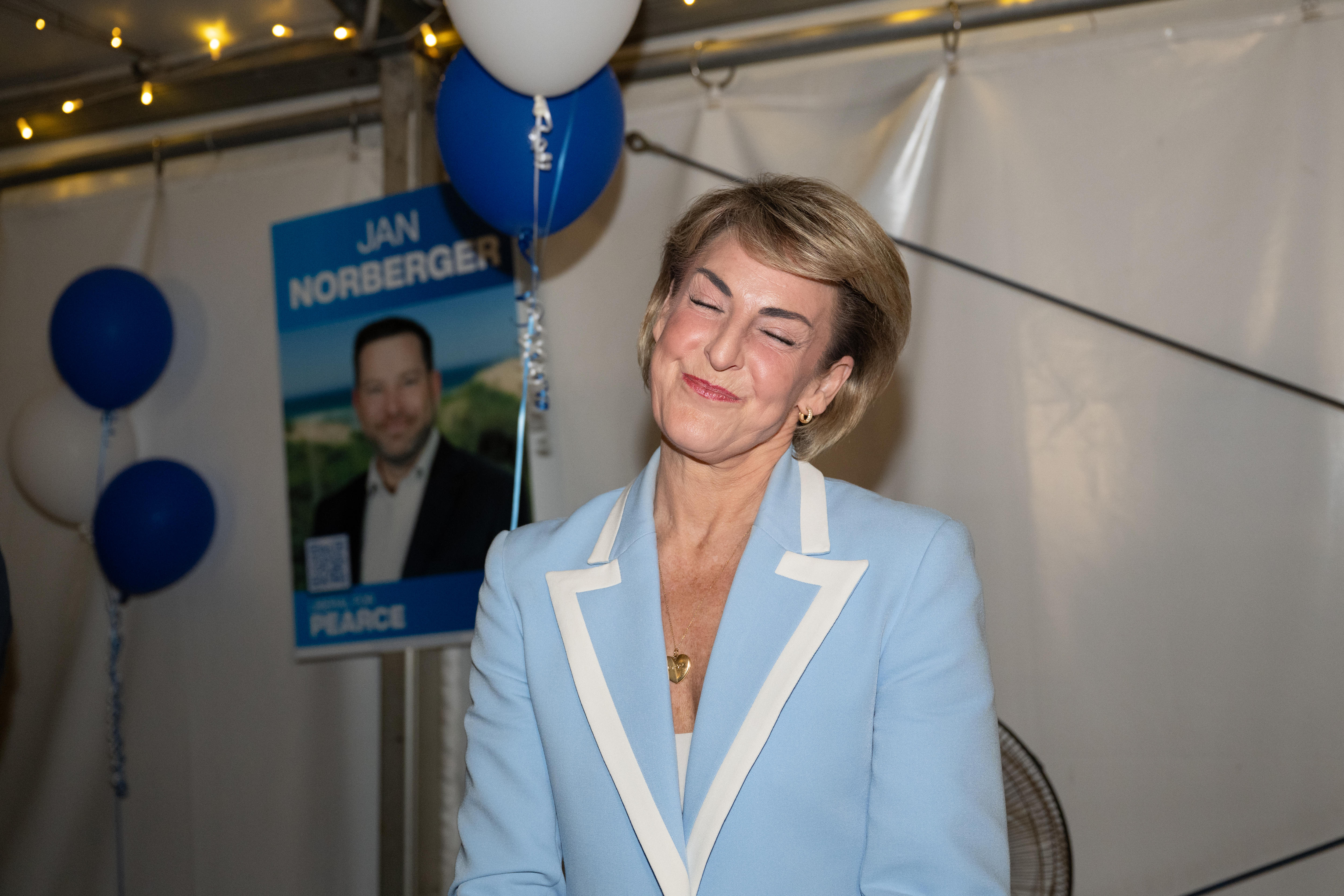 Michaelia Cash smiles with eyes closed and head to the side, liberal corflute behind her