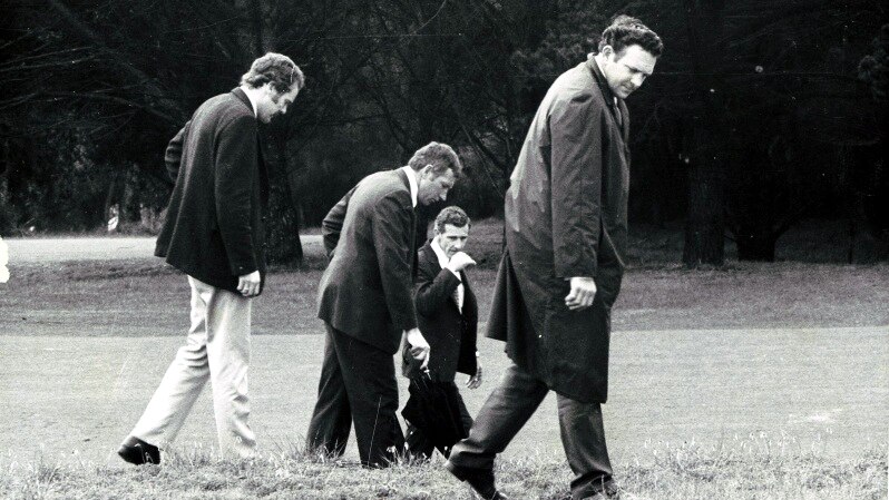 A black and white photo of four men with their heads down looking at the grass