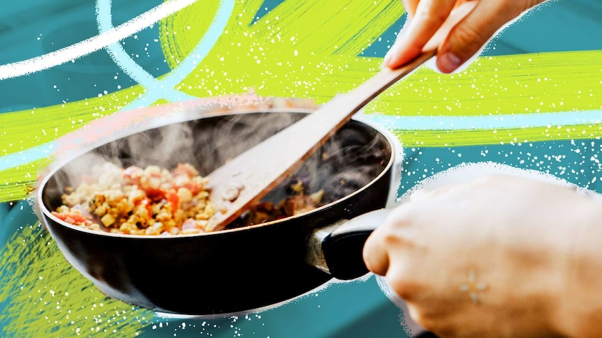 A person holds a steaming frypan, stirring it with a wooden spoon, making a light stir fry for dinner.