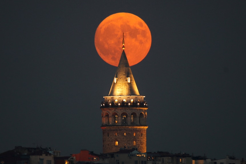 An orange moon appears behind a tower.