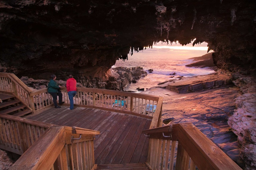 An arched rock formation with sea behind and a boardwalk in the foreground with two people on it