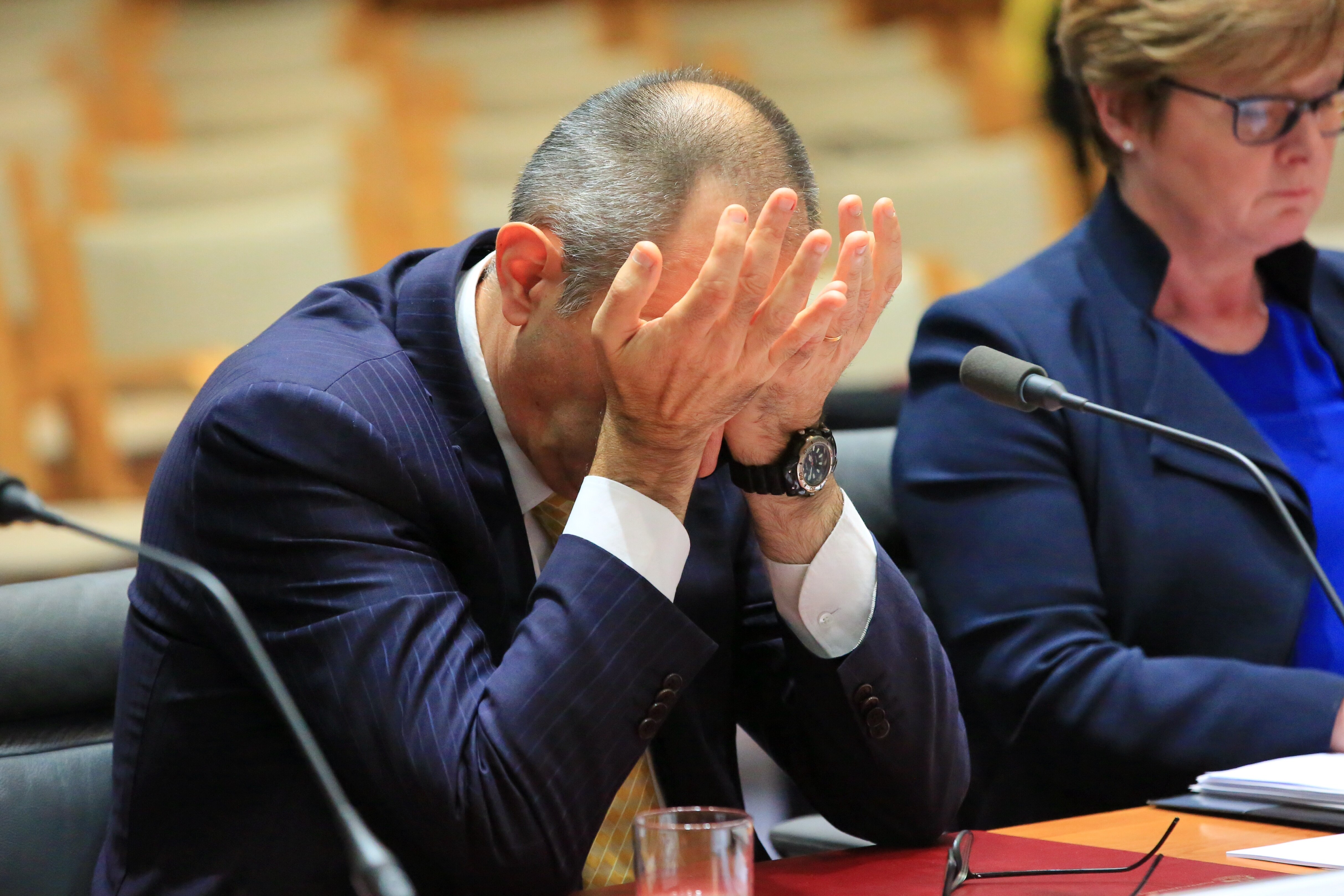 Mike Pezzullo holds his head in his hands during a senate estimates hearing