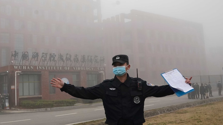 A security person moves journalists away from the Wuhan Institute of Virology