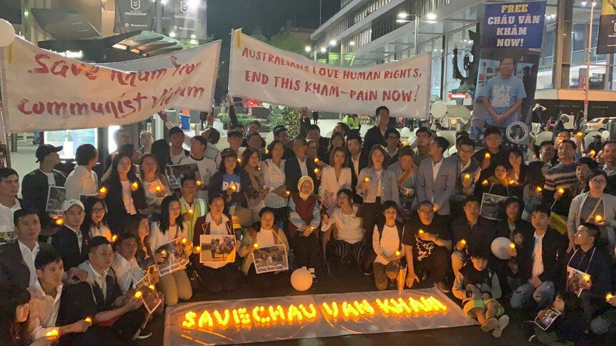 A group of people hold candles with banners at night holding posters.