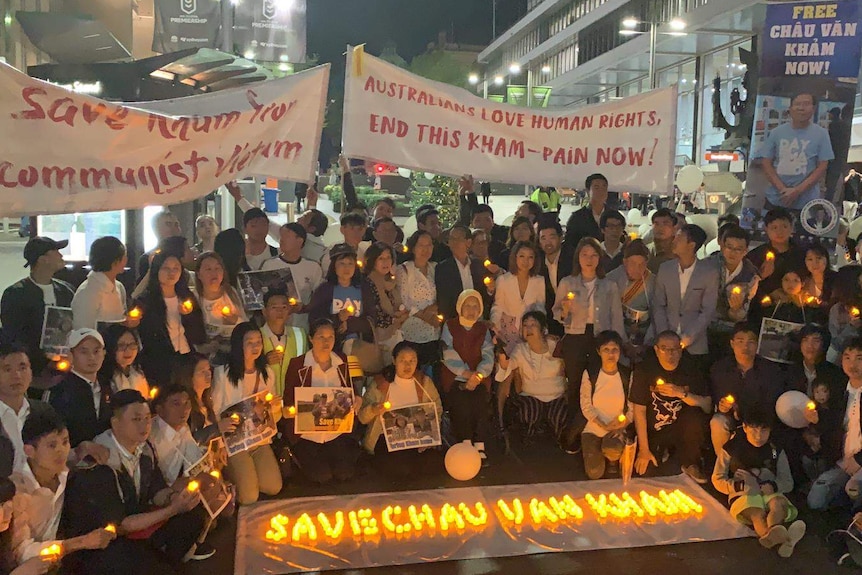 A group of people hold candles with banners at night holding posters.