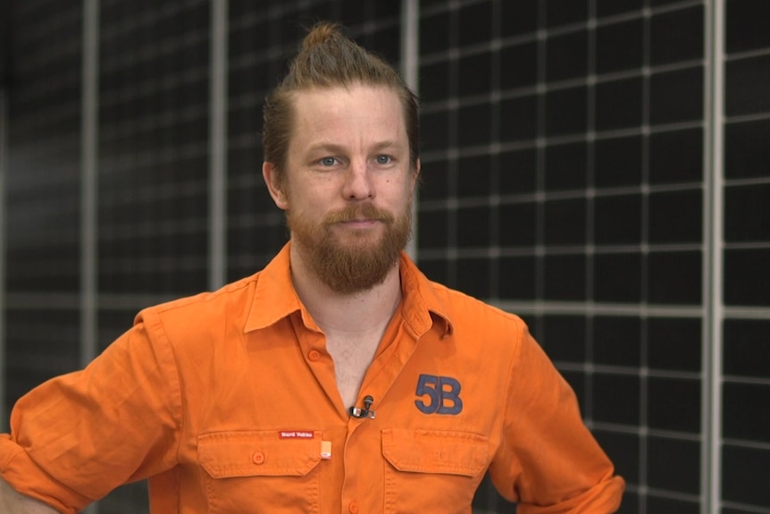 Un homme de race blanche avec une barbe, portant un gilet orange haute visibilité 