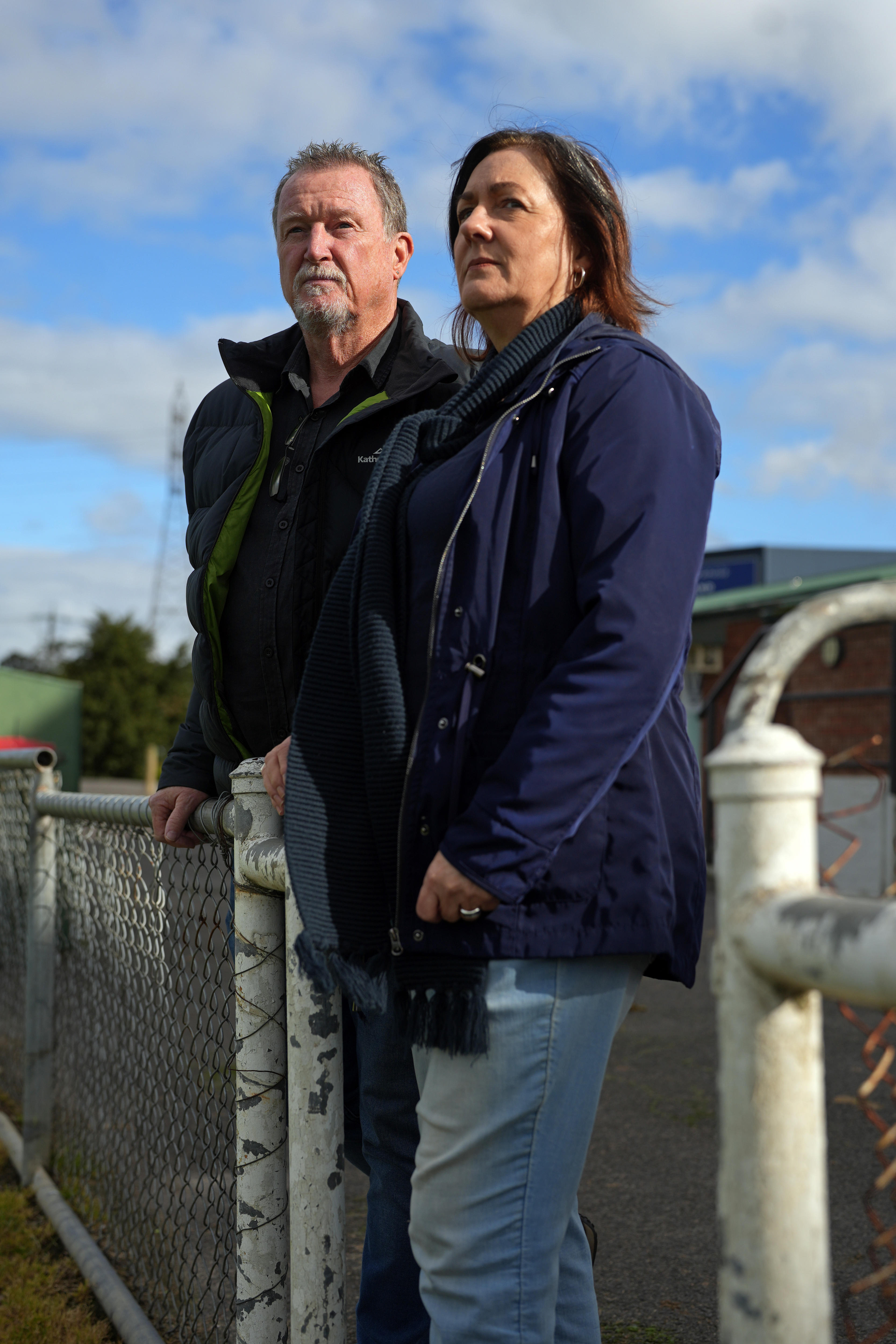 A man and a woman stand leaning on a low fence at a sports oval.