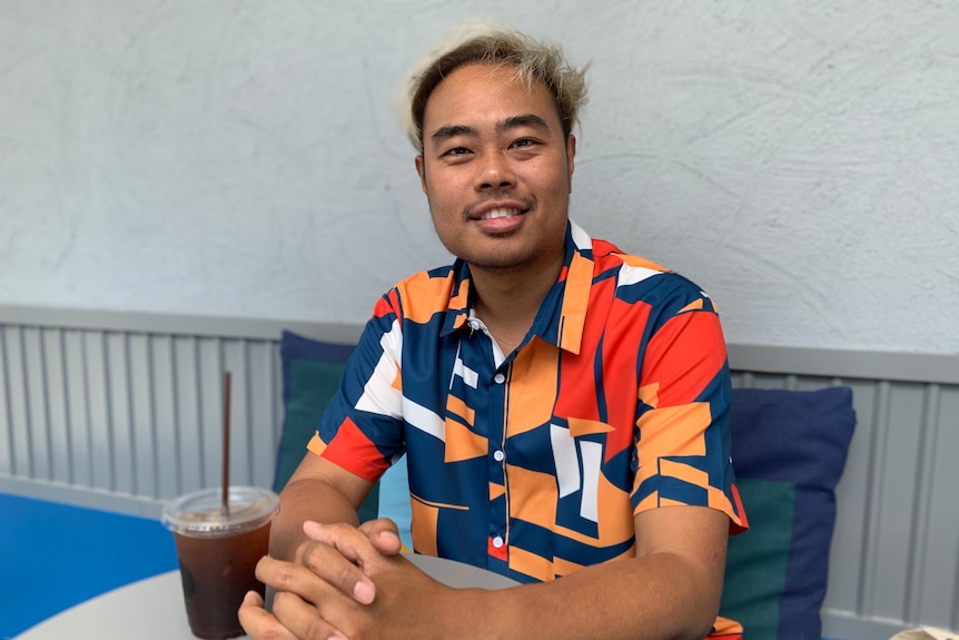 A young Thai man with bleached blonde hair and a colourful shirt smiles 
