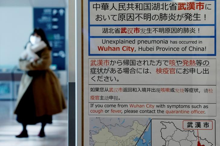 A woman in a face mask walks behind a sign reading 'unexplained pneumonia in Wuhan'