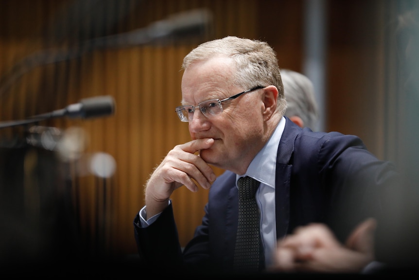 Philip Lowe giving evidence, resting his head on his hand.