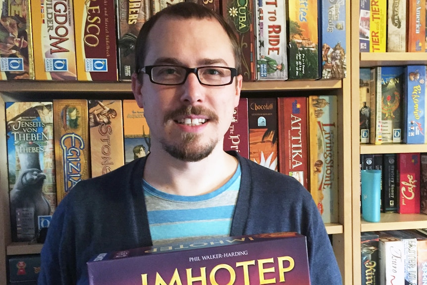 Board game designer and Anglican pastor Phil Walker-Harding, holding his game Imhotep.