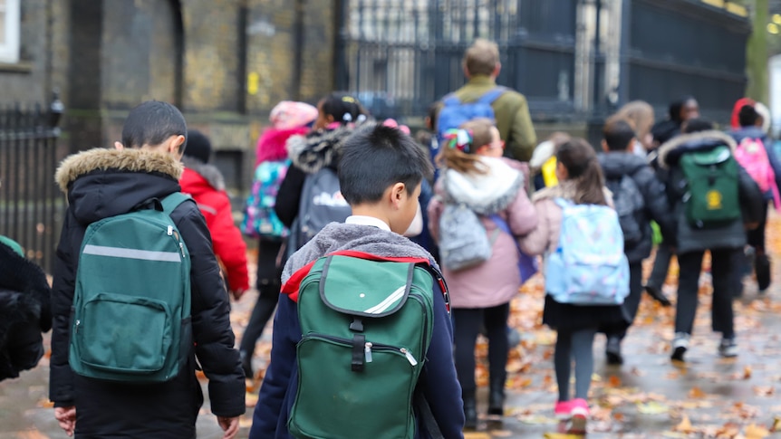 Primary school kids carrying backpacks on a rainy winter day.