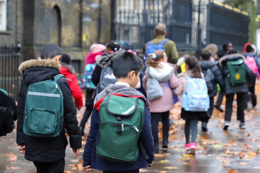 Primary school kids carrying backpacks on a rainy winter day.