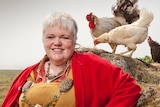 Icelandic priestess dressed in traditional clothing, holding a bull horn, with chickens behind her.