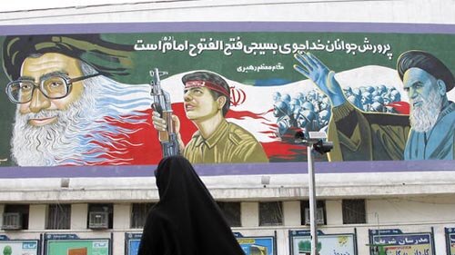 An Iranian woman crosses a street in front of a huge mural painting depicting Iran's supreme leader, Ayatollah Ali Khamenei