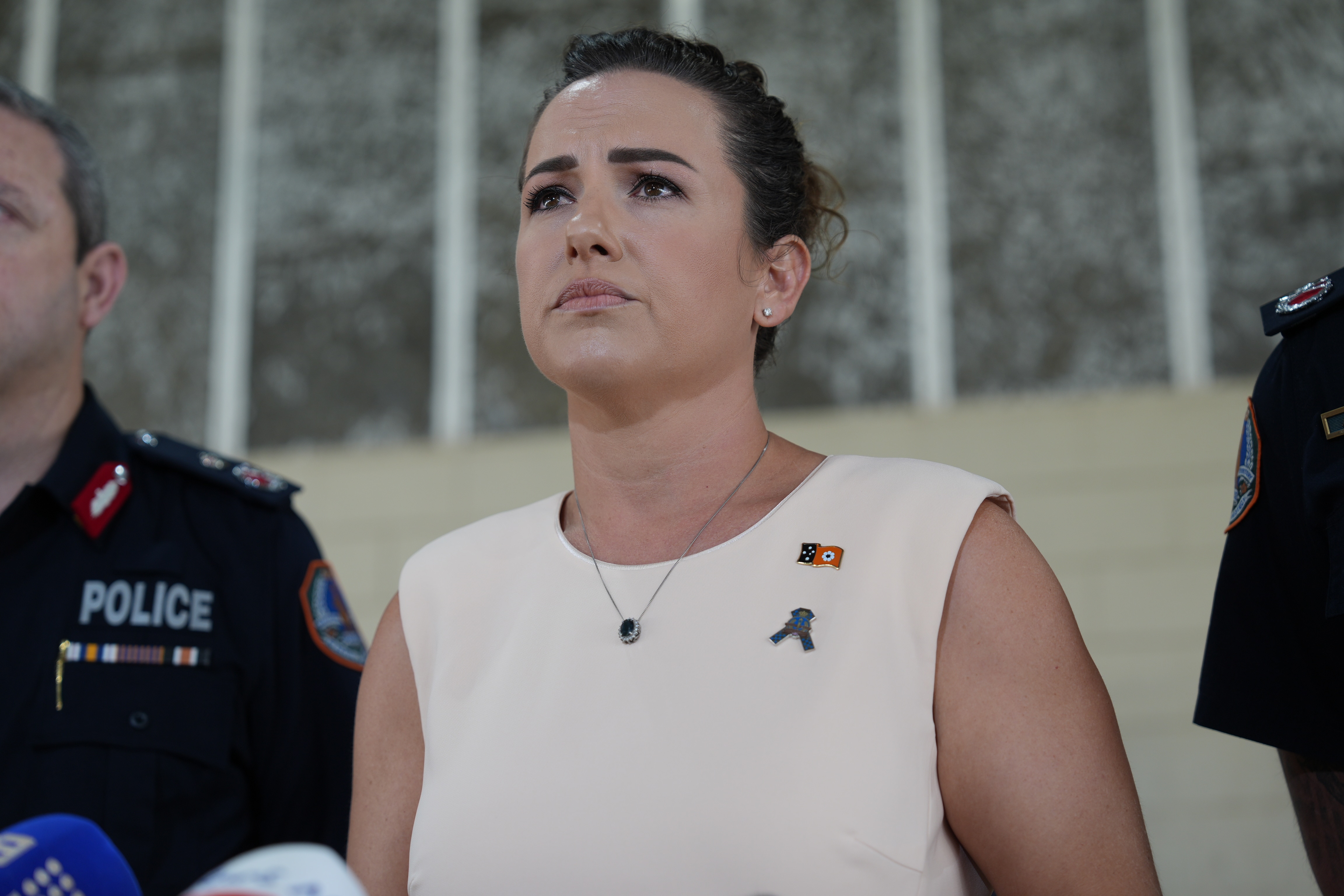 Lia Finocchiaro wearing a light pink dress with police officers standing either side of her.
