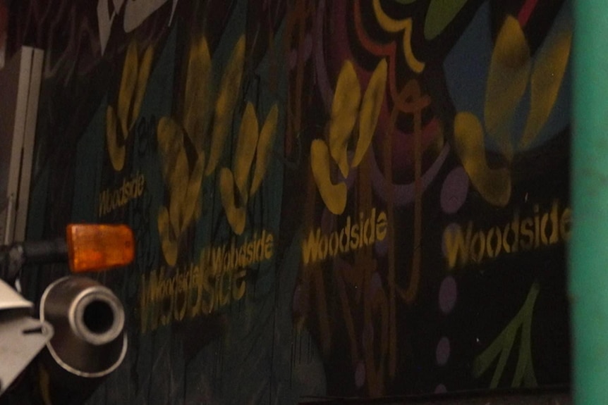 A repeated logo and the word 'Woodside' can be seen in yellow paint on a wall