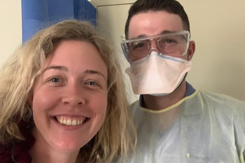 Bridget Wilkins standing with a doctor? in protective eyewear, gown and mask.