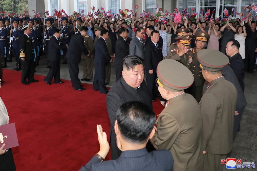 Kim Jong Un and officials shake hands on a red carpet. 