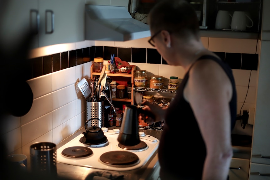 Steph holds a coffee put in her kitchen, above a stove with cutlery and cooking ingredients in the background.