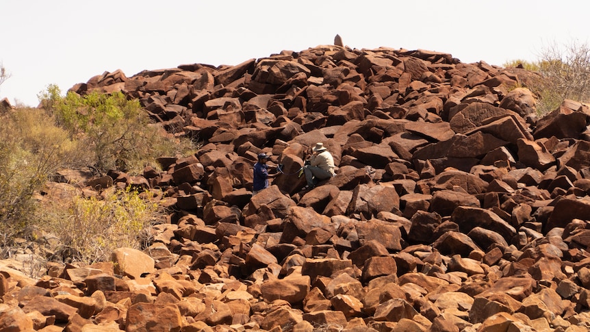 Two men work on a large rock formation.