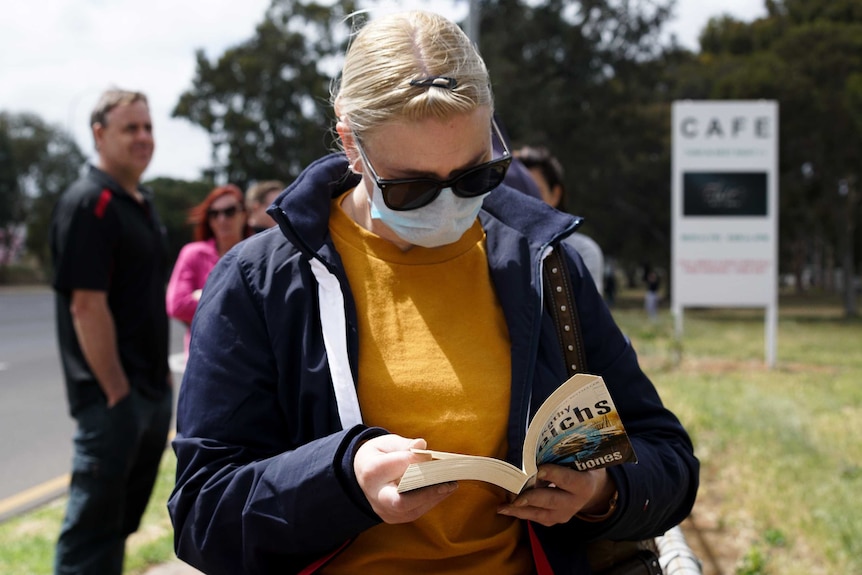 A woman reads a book as she waits in line for a COVID-19 test