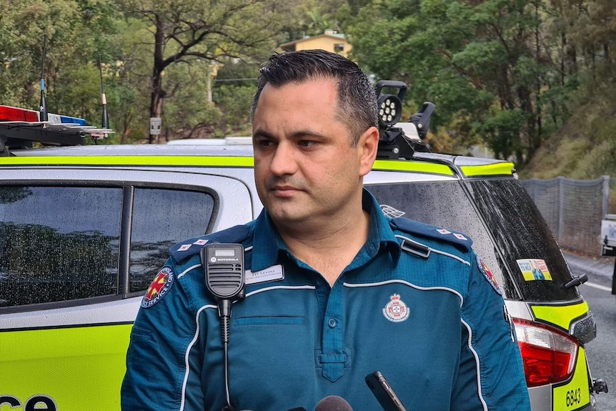 Queensland Ambulance Service acting operations supervisor Jay Nevins talks to media in front of police car.