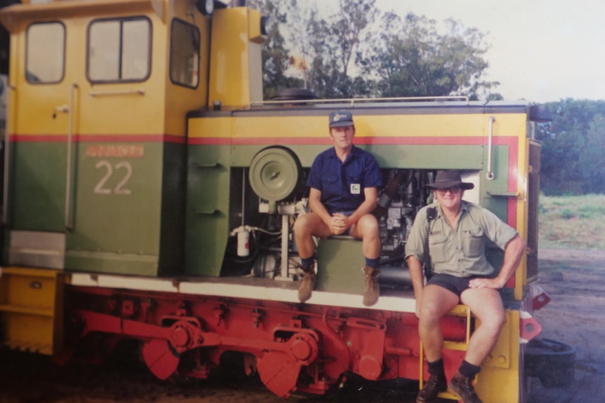 two men sit on a yellow and green loco