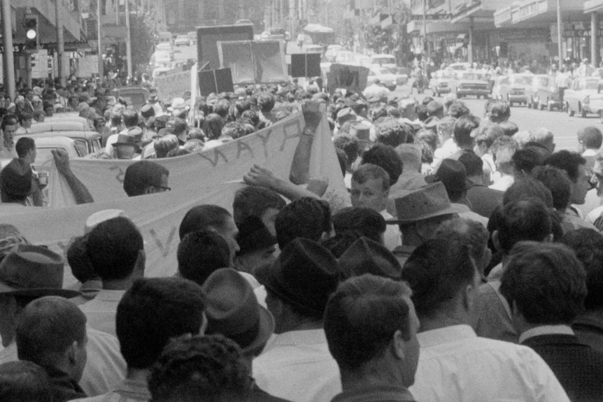 A black-and-white historical image of a large group of people marching down a busy street to protest against capital punishment.