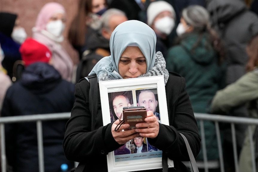 A Syrian woman stands outside court in Germany holding pictures of her five brothers who died in Syria.