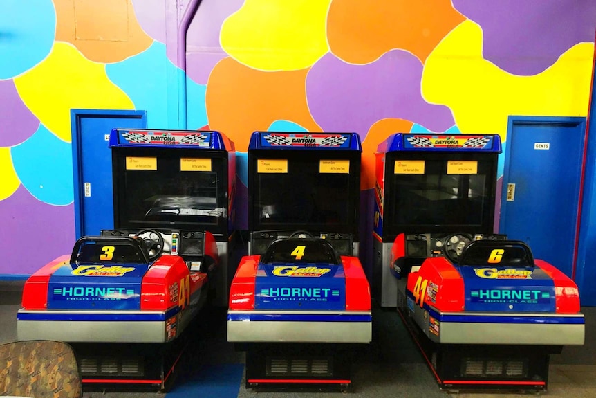 Photograph of three computer games in front of a brightly coloured wall with a toilet door on either side.