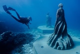 A scuba diver swims beside an underwater statue of a human figure 