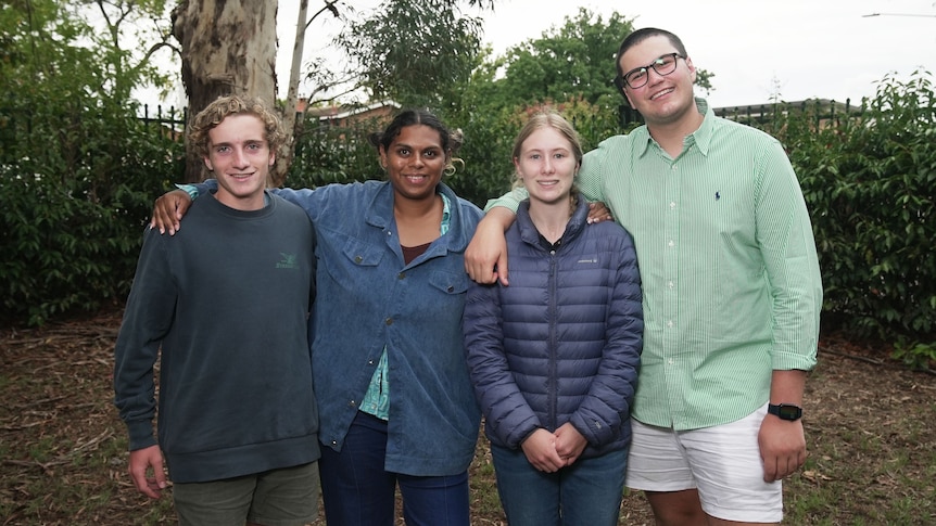 Four people stand side by side with arms over shoulders smiling.