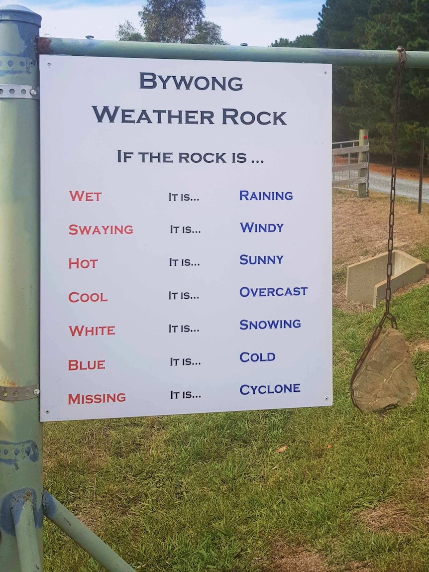 A rock hangs from a pole, with a sign saying that if the rock is missing, there has been a cyclone.