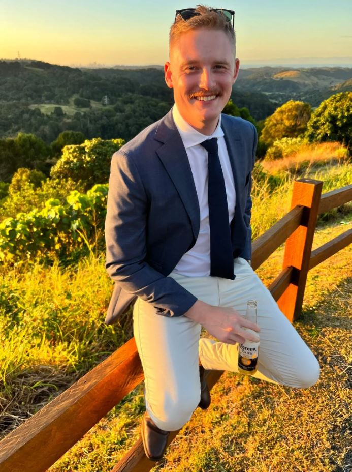 A man in a suit with rolling green hills behind him