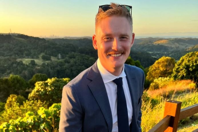 A man in a suit with rolling green hills behind him