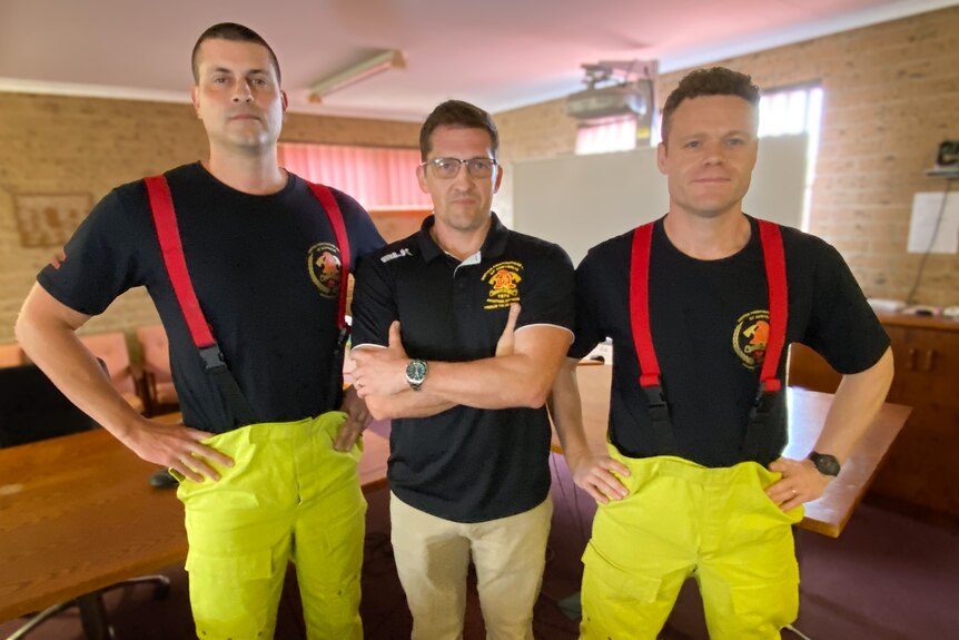 Wes Garrett stands with his arms crossed between two taller firefighters dressed in navy shirts.