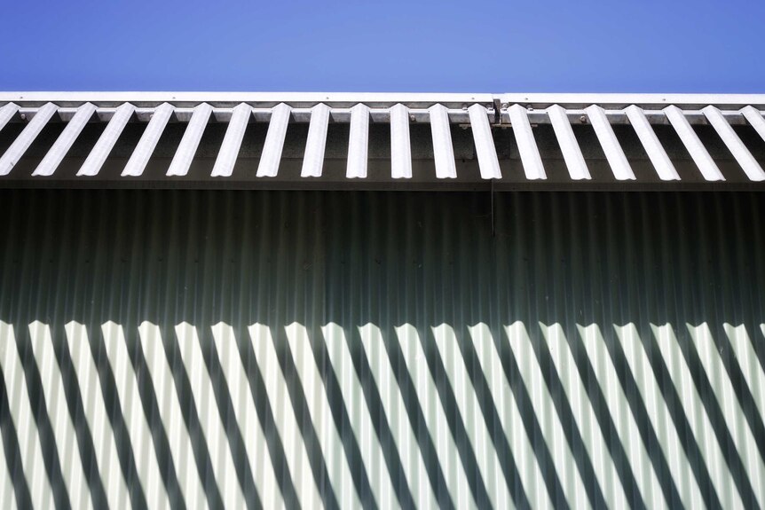 The top of a corrugated iron fence with protruding pieces of metal aimed at preventing escape.