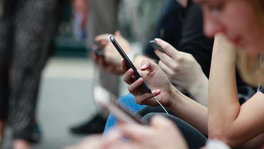 A group of people sitting, each holding and using a mobile phone