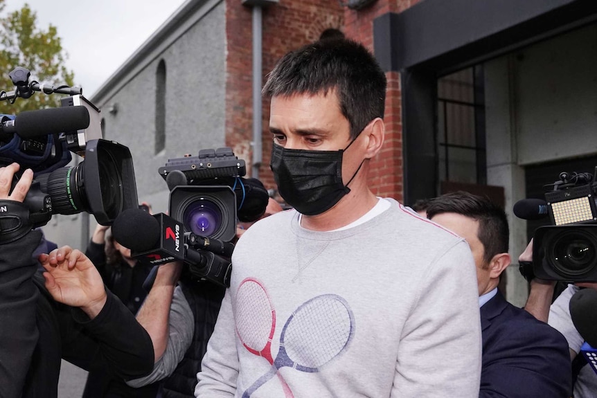 TV cameras video a man wearing a black mask as he is led out of a house.