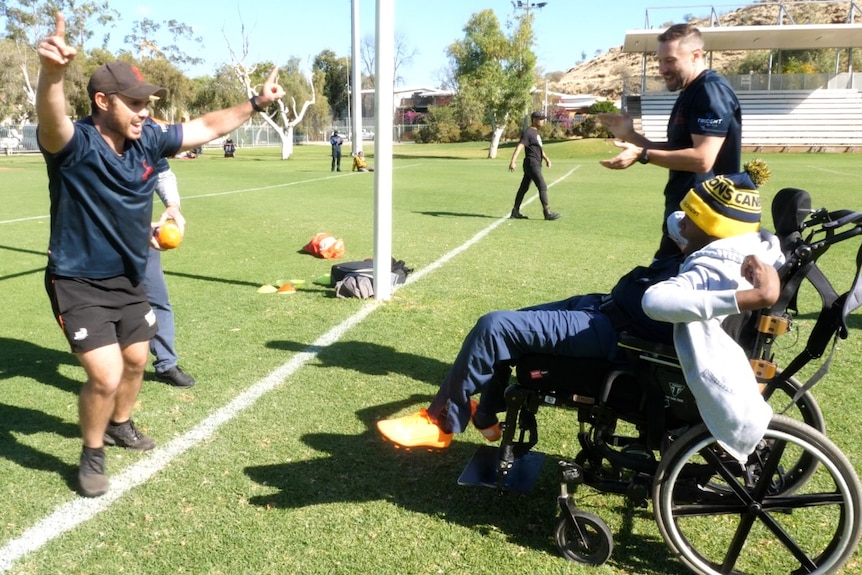 A coach holds his arms in the air to celebrate a goal kicked by a young man with cerebral palsy