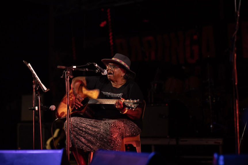 A woman playing guitar on a stage at barunga festival.